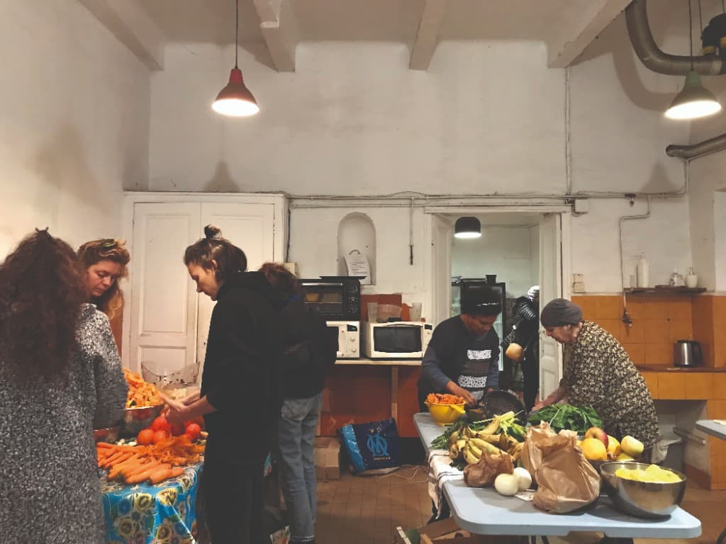 Plusieurs personnes épluchant et découpant des légumes frais dans la cuisine commune du jardin.
